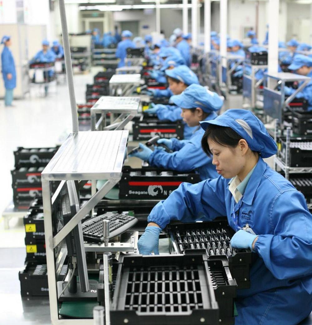 female factory workers in blue overalls sitting at workstations assembling products